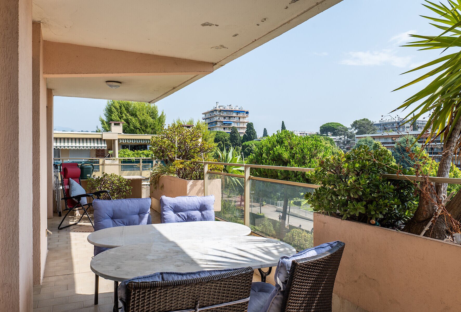 A balcony with a table and chairs, overlooking a cityscape with buildings and greenery.
