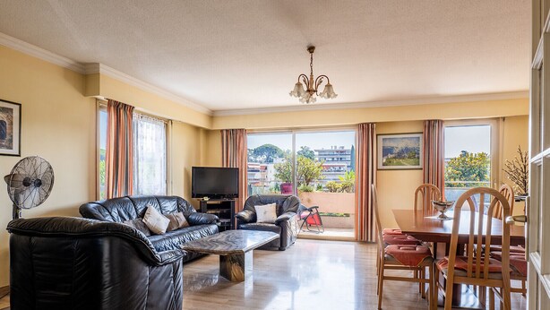 A living room with a sofa, TV, and dining area with chairs and a table. - Flat with swimming pool close to the sea (Cagnes-sur-Mer)
