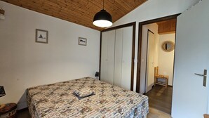 A bedroom with a bed covered in a patterned bedspread, a wooden ceiling, and a door leading to another room.
