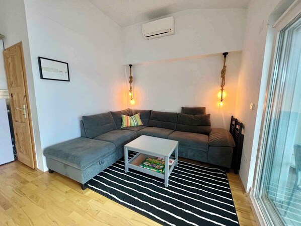Una sala de estar moderna con un sofá seccional gris, una mesa de centro blanca y un tapete a rayas negro y blanco. Hay dos lámparas de pared y un cuadro en la pared.