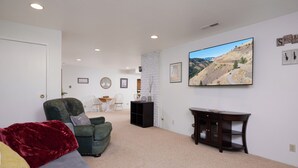 A living room with a green sofa, a red throw blanket, a flat-screen TV, and a bookshelf. - ESCAPE TO WALLA WALLA WINE COUNTRY — YOUR PRIVATE KING SUITE ACROSS FROM TH... (College Place)