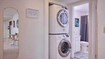 A laundry room with two stacked washers and dryers, a mirror, a framed inspirational quote, and a view into the bathroom.
