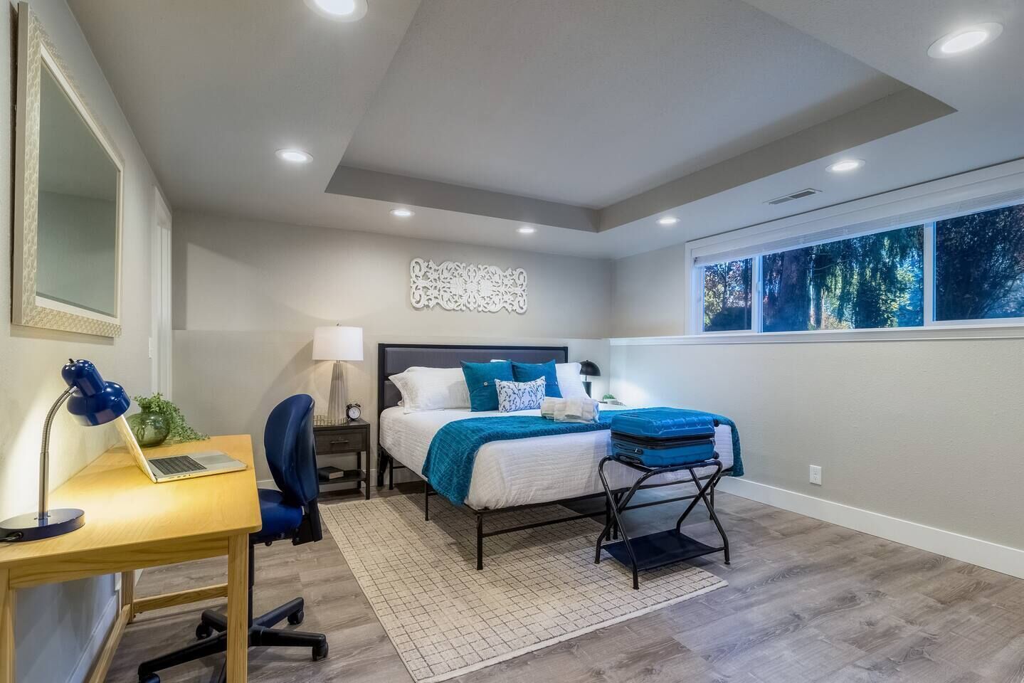 Une chambre à coucher comprenant un lit, un bureau, une chaise et une fenêtre donnant sur des arbres.
