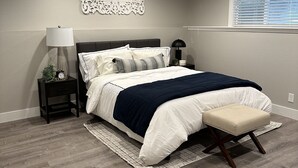 Un dormitorio con cama, mesitas de noche, lámpara, un adorno en la pared y una ventana con persianas.