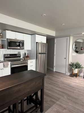 A modern kitchen with white cabinets, stainless steel appliances, and a wooden dining table.