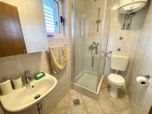 A bathroom with a sink, toilet, shower, and a glass-enclosed shower stall. - Holiday apartment with balcony and air conditioning (Jadranovo)