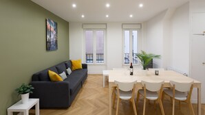 Ein modernes Wohnzimmer mit einem grauen Sofa, einem Esstisch mit Stühlen und einer Topfpflanze.