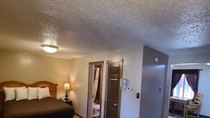 A hotel room with a bed, bedside table, lamp, and a bathroom door. - The B&B Motel (Lewistown)