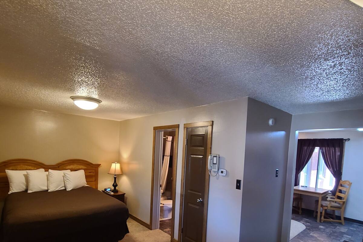 A hotel room with a bed, bedside table, lamp, and a bathroom door.