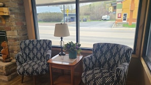 A room with two patterned armchairs, a small wooden table with a lamp and a potted plant, and a stone fireplace. - The B&B Motel (Lewistown)