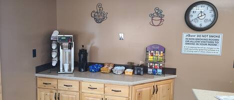 A kitchenette with a coffee machine, a clock, and a sign prohibiting smoking.
