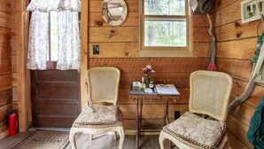 A wooden cabin interior with two wicker chairs, a small table with a vase, and a window with a view of trees. - Riverbright Treehouse on the Toccoa (Suches)