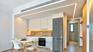 Une cuisine moderne avec des meubles blancs, un réfrigérateur en acier inoxydable et un coin repas comprenant une table et des chaises blanches.
