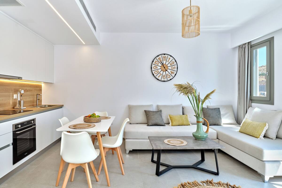 Una cocina moderna con armarios blancos, horno empotrado y un comedor con mesa y sillas blancas.