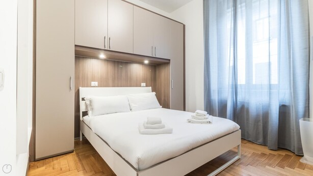 A modern bedroom with a bed, wooden headboard, and a large window with curtains. - Italianway Comfort - San Maurilio 20 B (Milan)