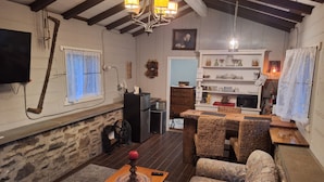 A cozy living room with a fireplace, a dining area with wicker furniture, and a kitchen with wooden cabinets and a hanging light fixture.