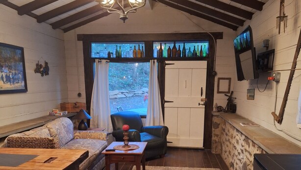 A cozy living room with a wooden dining table, a sofa, and a TV mounted on the wall.