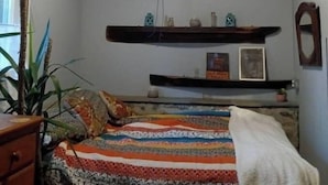 A bedroom with a wooden ceiling, a bed with a colorful quilt, and shelves with various items.