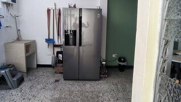A compact kitchen with a stainless steel refrigerator, a water dispenser, and a mop rack.