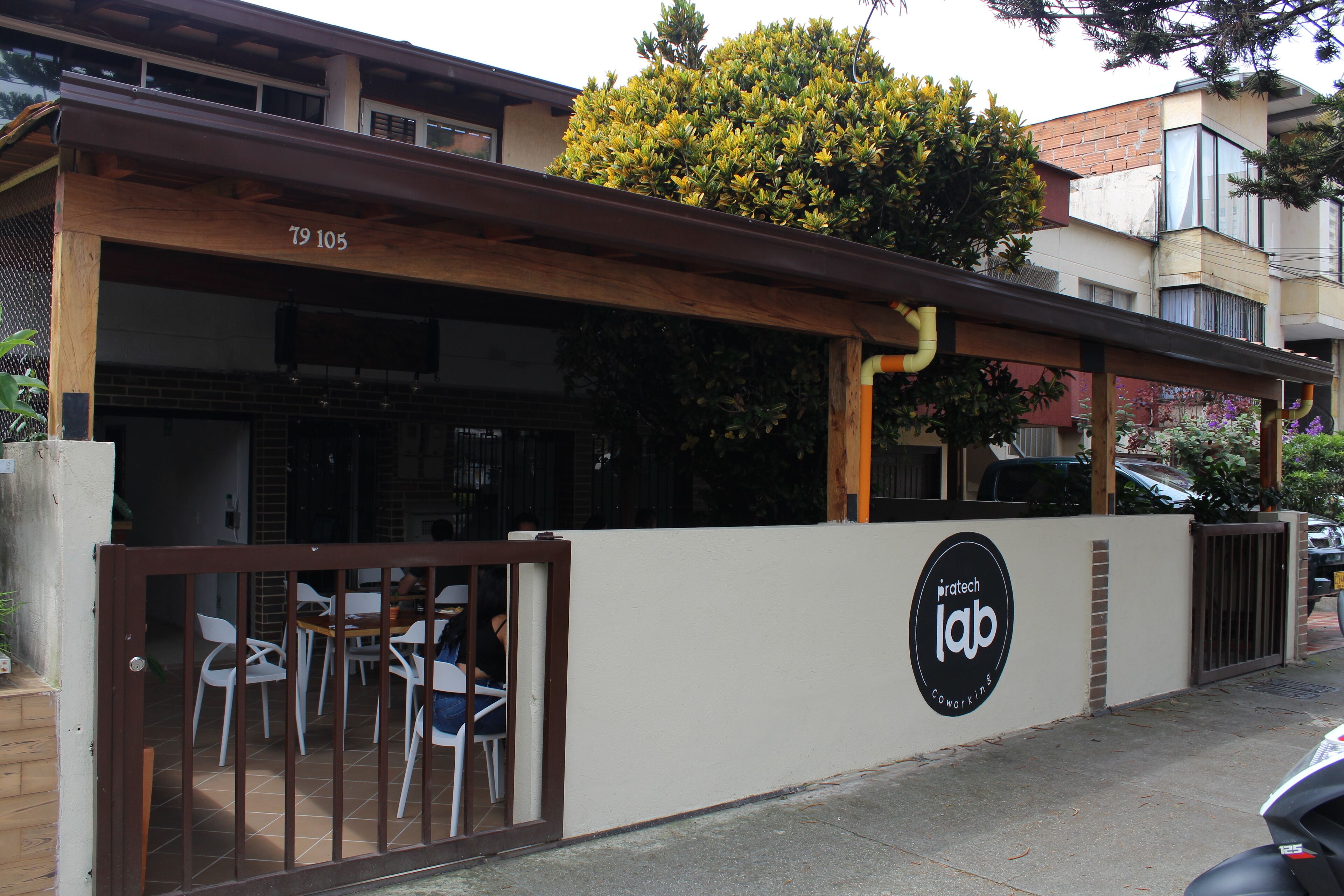 A building with a sign reading "pratech lab coworking" and a gated entrance with chairs outside.