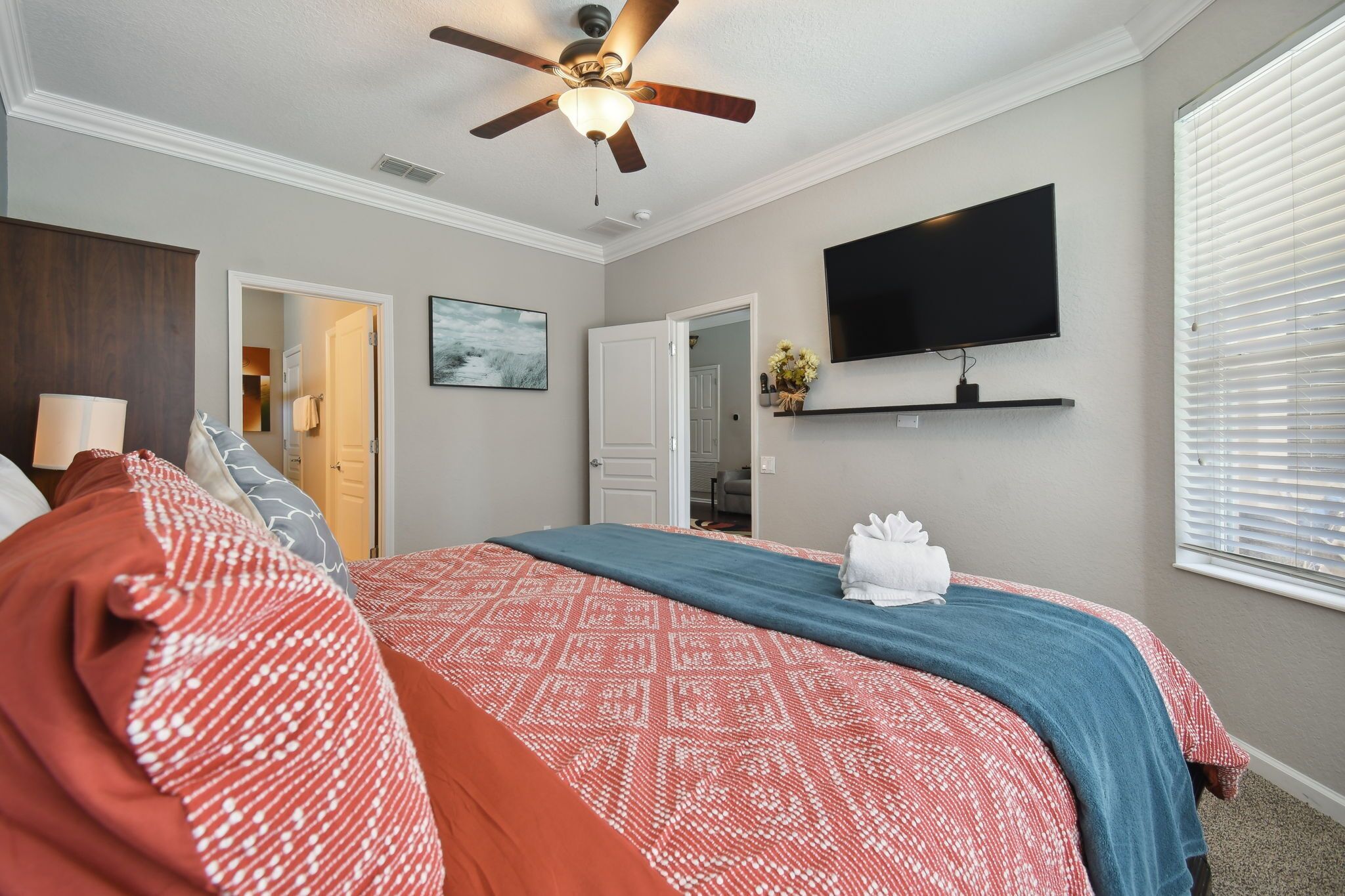 A bedroom with a bed, a ceiling fan, a TV on the wall, and a window with blinds.