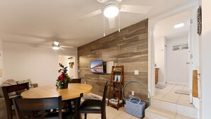 A dining area with a wooden table, chairs, a ceiling fan, and a television on the wall.