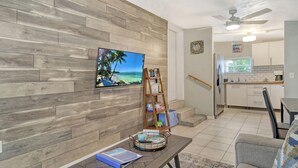 A modern living room with a wooden wall, a flat-screen TV, a coffee table, and a bookshelf.