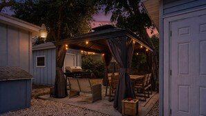 A covered outdoor patio with a grill, seating, and string lights.