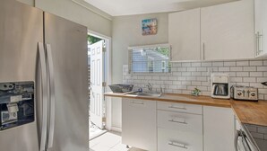 A modern kitchen with white cabinets, a stainless steel refrigerator, a sink, a toaster, and a window with blinds.