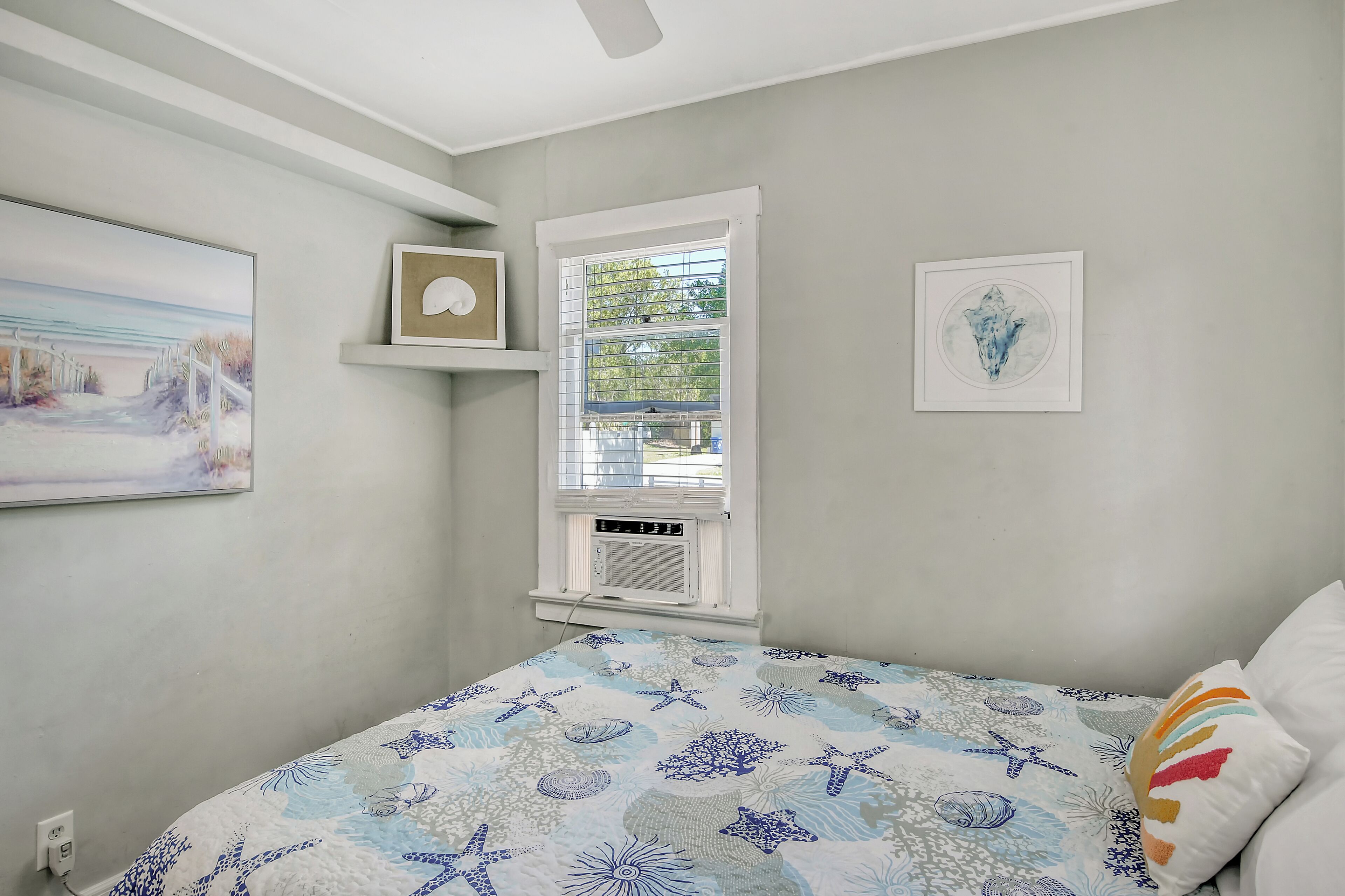 Ein Schlafzimmer mit einem Bett, einem Fenster mit Jalousien, einer Wand-Klimaanlage und einem gerahmten Bild.