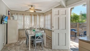 Uma sala de jantar com mesa e cadeiras, um ventilador de teto e vista para o pátio externo.