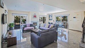 A spacious living area with a fireplace, two sofas, a coffee table, and a dining area with chairs. - Villa Delfini 1 (Paralimni)