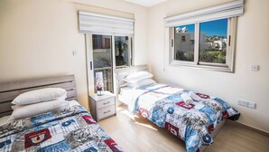 A bedroom with two beds, a window with a view, and a bedside table. - Villa Delfini 1 (Paralimni)