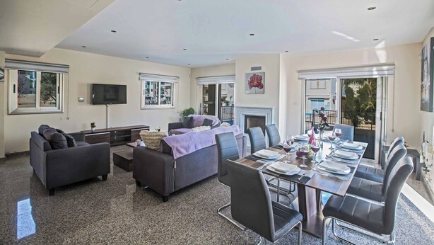 A spacious living area with a dining table set for six, a sofa, a TV, and a fireplace. - Villa Delfini 1 (Paralimni)