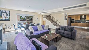 A spacious living room with a large sofa, a coffee table, and a staircase leading to an upper floor. - Villa Delfini 1 (Paralimni)