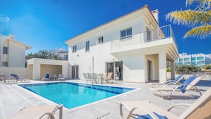 A swimming pool with lounge chairs and a building with balconies. - Villa Delfini 1 (Paralimni)