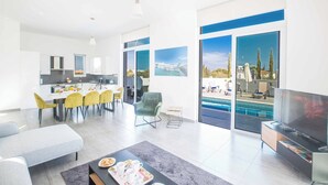 A modern living room with a dining area, a TV, and a pool view. - Villa Polymnia Protaras 1 (Paralimni)