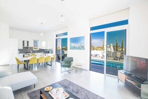 Ein modernes Wohnzimmer mit Essbereich, Fernseher und Blick auf einen Pool.