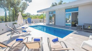 A modern outdoor pool area with lounge chairs and a dining area. - Villa Polymnia Protaras 1 (Paralimni)