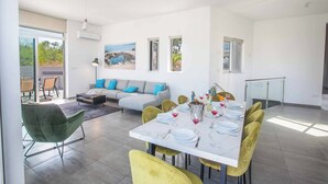A modern dining area with a marble table, yellow chairs, and a grey sofa with blue cushions. - Villa Polymnia Protaras 1 (Paralimni)
