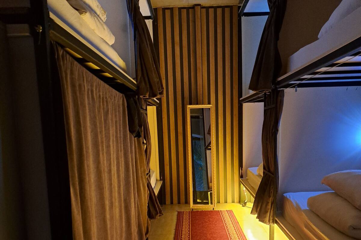 A narrow corridor with bunk beds on either side, a red patterned carpet, and a striped wall.