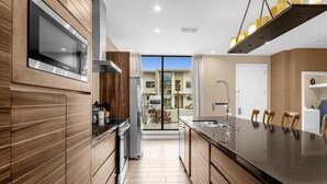 Une cuisine moderne avec des meubles en bois, un four à micro-ondes en acier inoxydable et un grand îlot central doté de tabourets de bar.