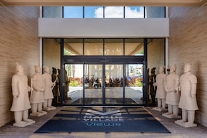 A modern entrance with glass doors, surrounded by stone statues, and a sign reading "Magic Village Views".