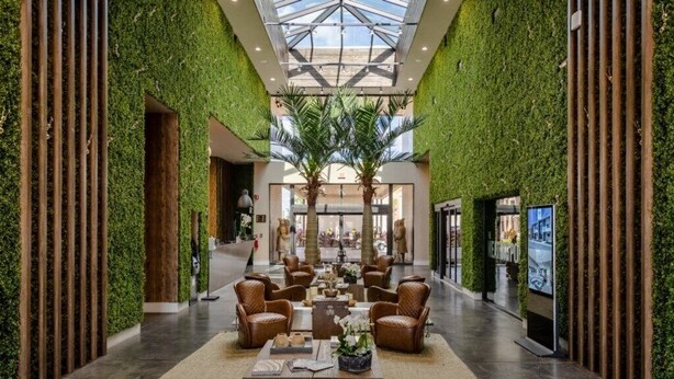 Un hall d’entrée spacieux avec un plafond haut, des murs agrémentés de plantes et un espace salon central.