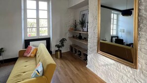 Un salon avec un canapé jaune, un grand miroir et un mur en briques blanches.