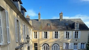Une cour avec un chemin de gravier menant à un bâtiment doté de nombreuses fenêtres et d’une porte.