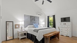 Een slaapkamer met een bed, nachtkastjes, een bankje, een kaptafel en een plafondventilator.