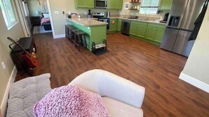 Una cocina amplia con armarios verdes, una isla central con taburetes, electrodomésticos de acero inoxidable y un ventilador de techo.