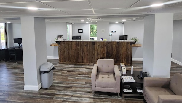 Zona de recepción con mostrador de madera, espacio de espera con una silla y un sofá, y un contenedor de basura.
