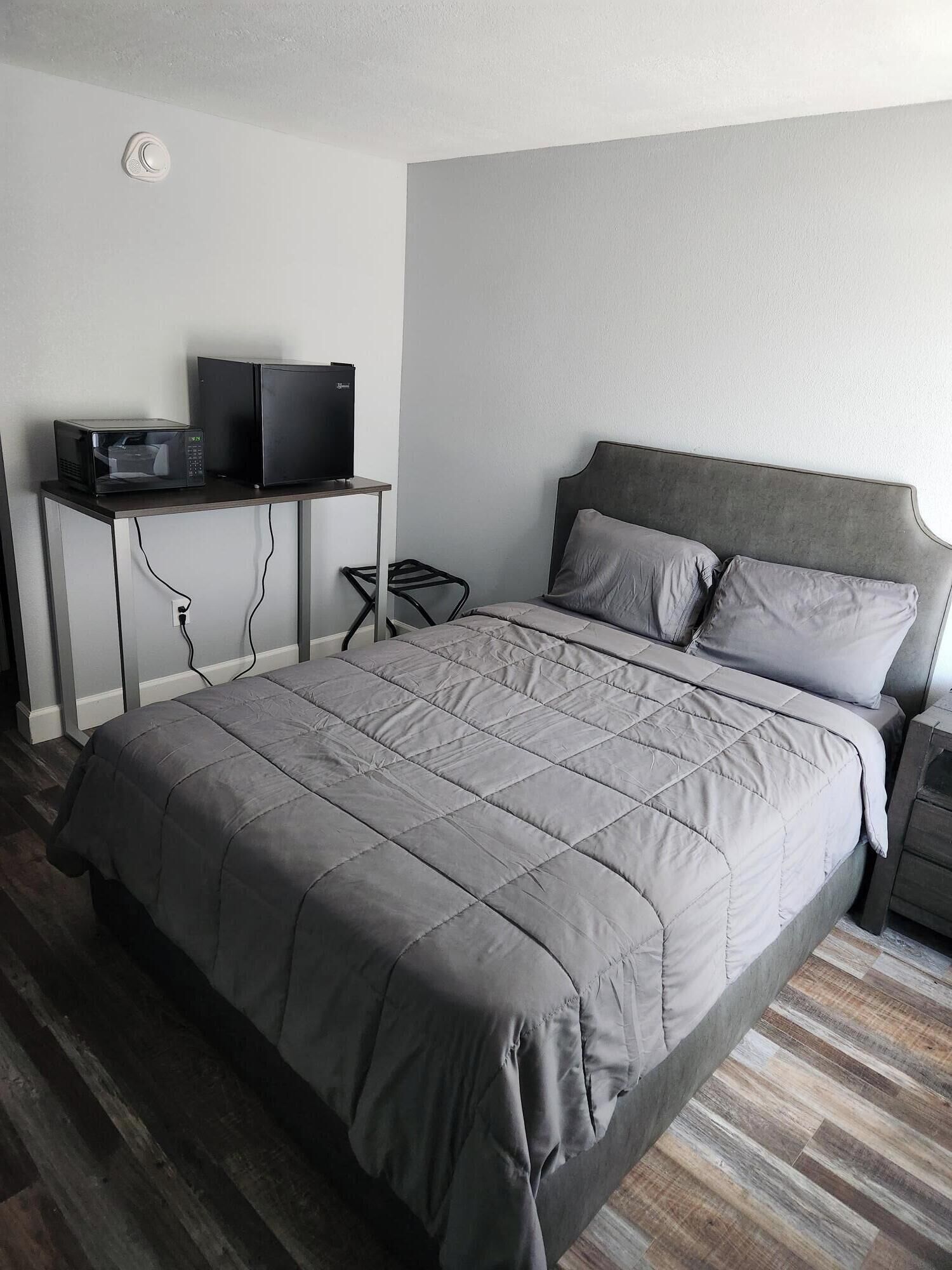 A bedroom with a bed, a desk with a microwave and a television, and a power outlet on the wall.